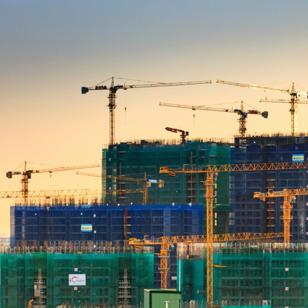 A cityscape featuring high-rise buildings under construction with cranes during sunset.