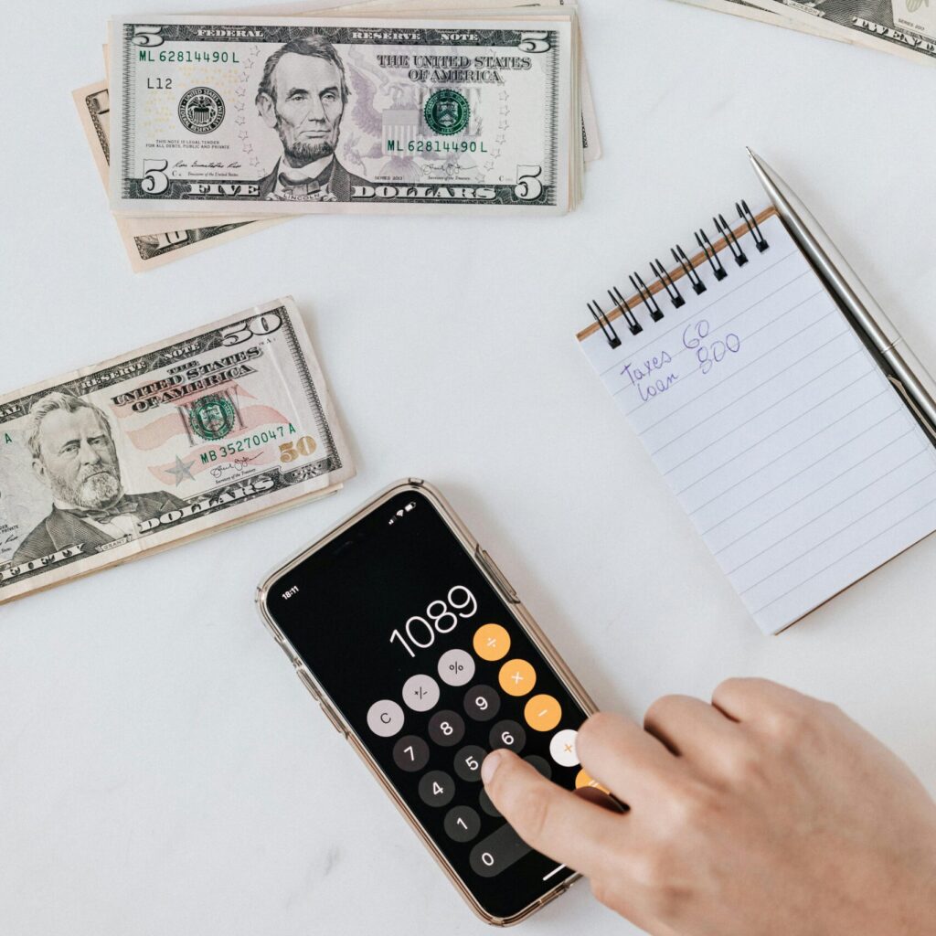 Overhead view of a hand using a calculator with US dollars and notes, representing finance and budgeting.